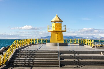 Historic yellow Hofoi lighthouse on the rocky shore of Reykjavik - obrazy, fototapety, plakaty