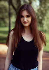 Beautiful toothy smiling teen woman looking happy outdoors in black t-shirt on summer green trees background. Closeup portrait in bright sunny day. Front view.