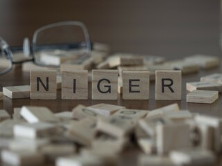 Niger word or concept represented by wooden letter tiles on a wooden table with glasses and a book