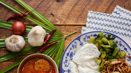Thai rice noodle with peanut sauce served in a white plate on a wooden table and decorated with leaves.