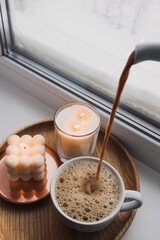 Pouring hot cocoa or coffee with milk in a cup.Winter still life with hot drink and candles