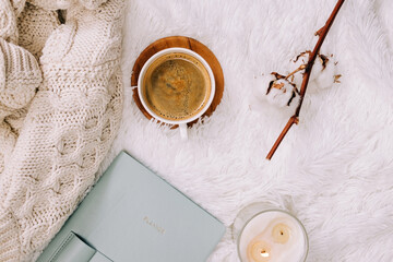 Flat lay with knitted warm sweater, candle and coffee on the bed.