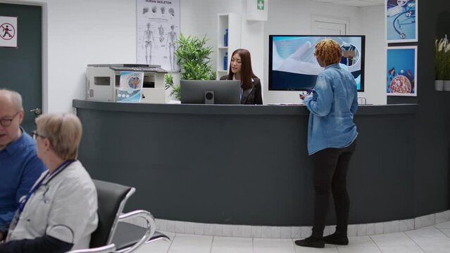 Female patient paying consultation with credit card at reception desk, attending checkup visit appointment. Woman talking to receptionist to pay medical consultation at clinical counter.