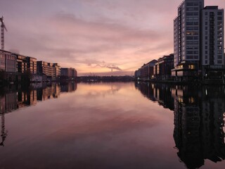 Buildings reflecting on a canal at sunset with industrial smoke in the distance in Dublin, Ireland