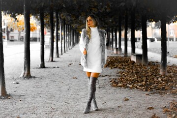 Beautiful young blonde woman in a white dress and gray knee-high boots taking a walk in a park