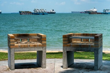 Two barbecue pits at tropical East Coast Beach in Singapore - Ships on background