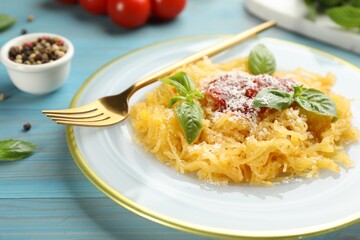 Tasty spaghetti squash with tomato sauce, cheese and basil served on light blue wooden table, closeup