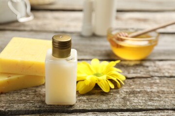 Bottle of cosmetic product and natural beeswax on wooden table, closeup