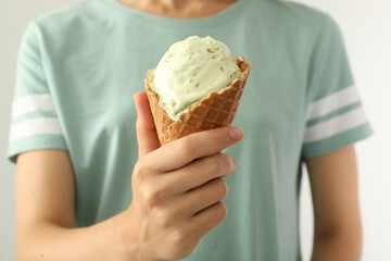 Woman holding green ice cream in wafer cone on light background, closeup