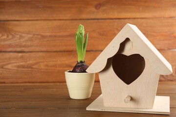 Beautiful bird house and potted hyacinth flower on wooden table, space for text