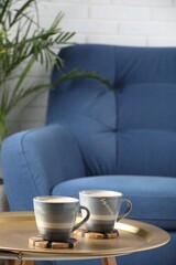Mugs of coffee with stylish cup coasters on metal table in room