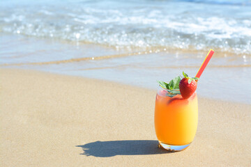 Glass of refreshing drink with strawberry on sandy beach near sea, space for text
