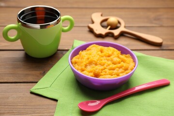 Plastic dishware with healthy baby food on wooden table