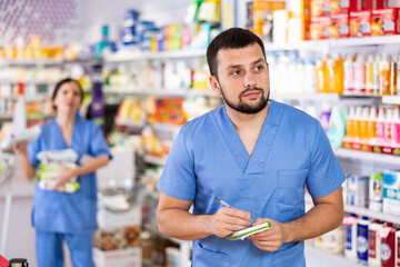 Diligent friendly male pharmacist noting assortment of drugs in pharmacy