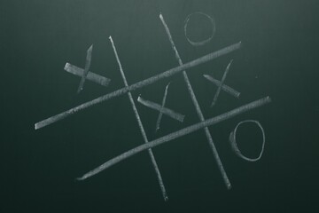 Tic tac toe game on green chalkboard, top view