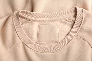Blank clothing label on beige sweater, top view
