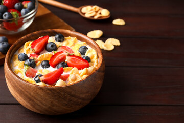 Bowl of tasty crispy corn flakes with milk and berries on wooden table. Space for text