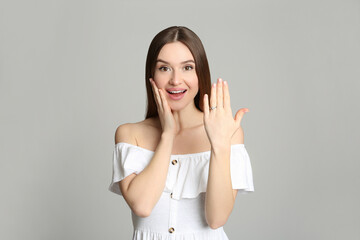 Happy young woman wearing beautiful engagement ring on grey background