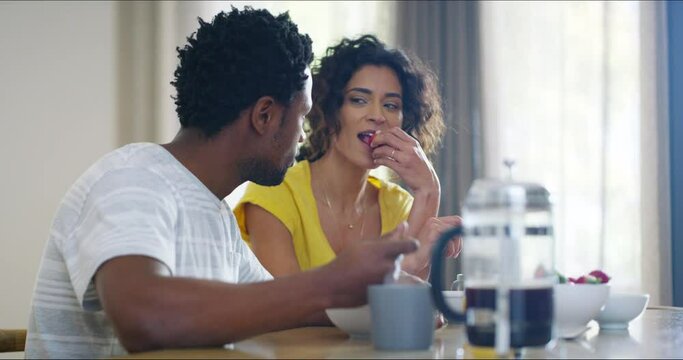 Cheerful, smiling and carefree boyfriend and flirty girlfriend enjoying good food, lunch or a snack at home. Interracial couple eating healthy breakfast, bonding and laughing together in the morning