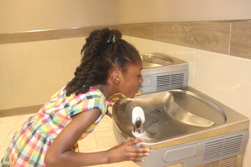 African American Kid drinking from water fountain indoors  - Powered by Adobe