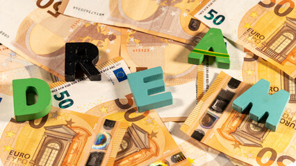 Message "dream" in colorful wooden letters, on a pile of fifty euro notes. European currency.