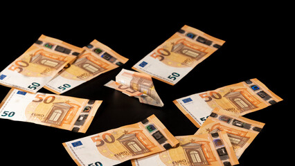 Banknote folded in the shape of an airplane, in the middle of fifty euro banknotes, on a black background. big plan