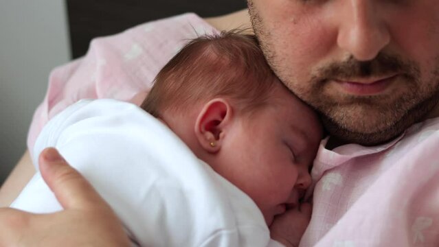 Close up of new father holding baby daughter as she sleeps on his chest