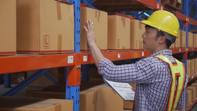 Young man applying shipping label to packaging or package and check document on clipboard in the warehouse at factory, worker writing and inspection manufacturing, logistic and shipping concept.