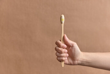 Hand holding an ecological bamboo toothbrush. Concepts: sustainability, use of compostable and environmentally friendly materials, zero plastics. Studio shot with copy space.