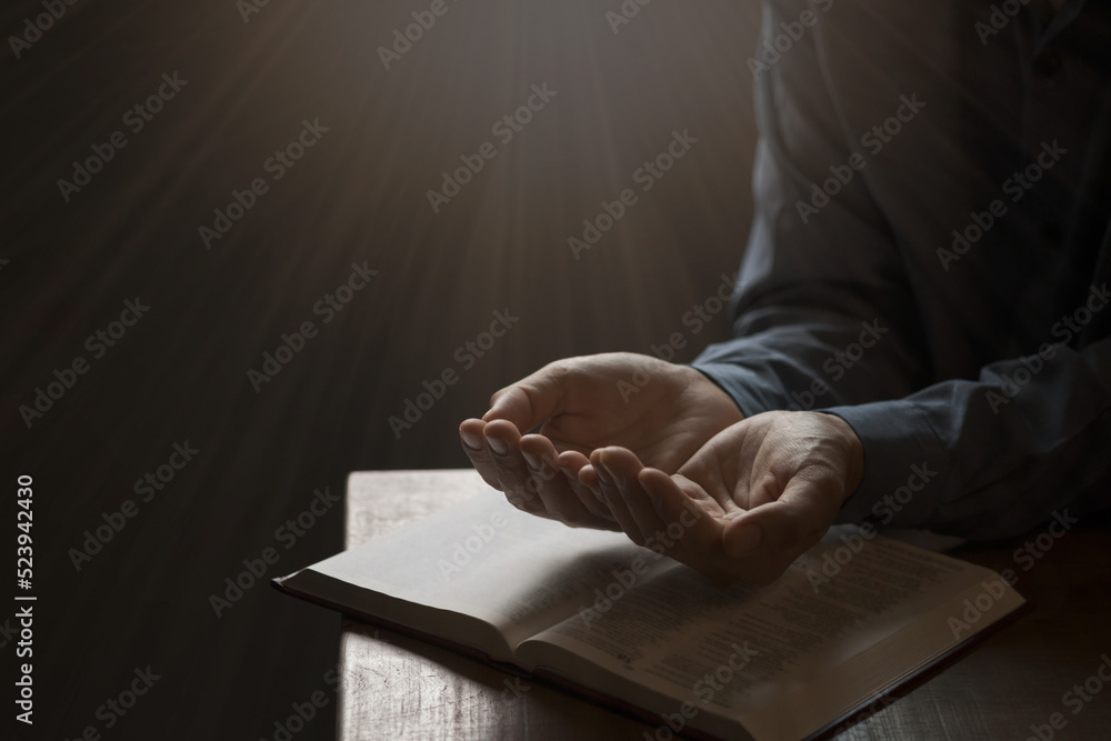 Wall mural man praying on holy bible in the morning have a yellow lights and sparkles coming. woman hand with b