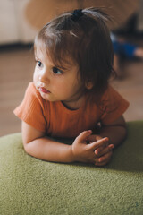 Baby girl pretty face with beautiful deep eyes looking away while sitting on the floor leaning on green sofa. Relax and peace. Innocent infant expression