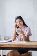 Young Asian Businesswoman using a mobile phone and works on a laptop computer in the modern home workplace office