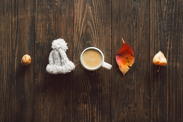 Autumn composition. Cup of coffee and autumn dried leaves, knitted little hat on wood background....