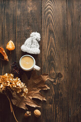 Autumn composition. Cup of coffee and autumn dried leaves, knitted little hat on wood background. Flat lay, top view
