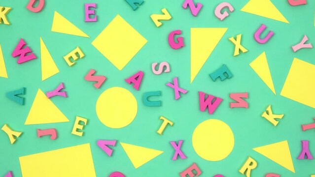 yellow geometric shapes and colored letters of the alphabet randomly lie on a rotating green background. primary education. creative minimalistic concept back to school. closeup. top view. 4k.