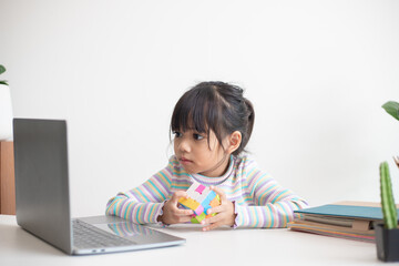 NAKHON RATCHASIMA, THAILAND - JULY 14, 2022:Asian little cute girl holding Rubik's cube in her hands. Rubik's cube is a game that increases the intelligence of children.