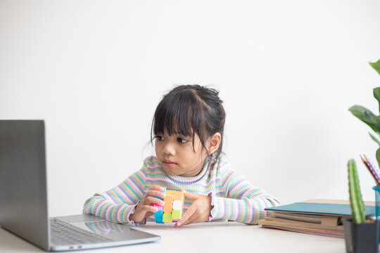 NAKHON RATCHASIMA, THAILAND - JULY 14, 2022:Asian little cute girl holding Rubik's cube in her hands. Rubik's cube is a game that increases the intelligence of children.