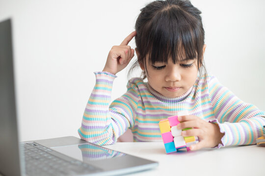 NAKHON RATCHASIMA, THAILAND - JULY 14, 2022:Asian little cute girl holding Rubik's cube in her hands. Rubik's cube is a game that increases the intelligence of children.
