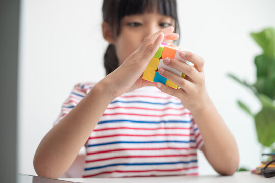 NAKHON RATCHASIMA, THAILAND - JULY 14, 2022:Asian little cute girl holding Rubik's cube in her hands. Rubik's cube is a game that increases the intelligence of children.