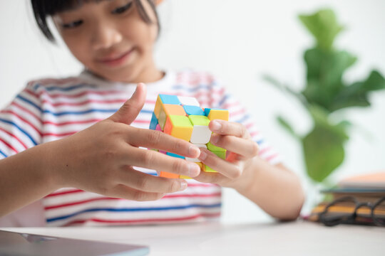 NAKHON RATCHASIMA, THAILAND - JULY 14, 2022:Asian little cute girl holding Rubik's cube in her hands. Rubik's cube is a game that increases the intelligence of children.