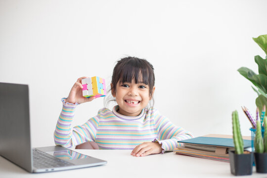 NAKHON RATCHASIMA, THAILAND - JULY 14, 2022:Asian little cute girl holding Rubik's cube in her hands. Rubik's cube is a game that increases the intelligence of children.