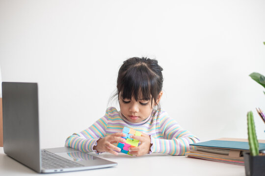 NAKHON RATCHASIMA, THAILAND - JULY 14, 2022:Asian little cute girl holding Rubik's cube in her hands. Rubik's cube is a game that increases the intelligence of children.