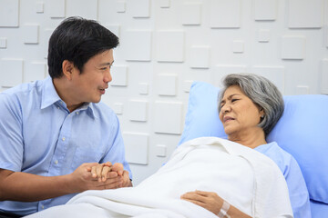 Fototapeta premium Senior Asian female patient resting on the medical bed in hospital and talking to doctor. 