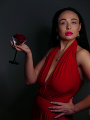 brunette with red lipstick on her lips in a red dress with red stones in jewelry with a red rose in...