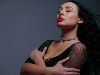 brunette with red lipstick on her lips in a black bodysuit on a gray background
