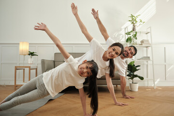 Asian Thai parents and daughter fitness training exercise and practice yoga on living room floor, lovely rowing together for health and wellness, and happy domestic home lifestyle on family weekend.