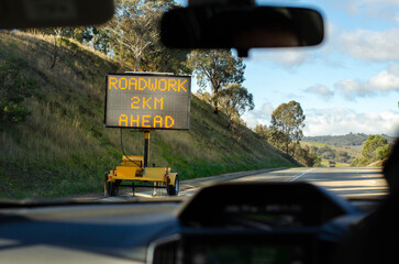 Electronic screen road sign with text .'roadwork 2km ahead' on side of an Australian country highway.
