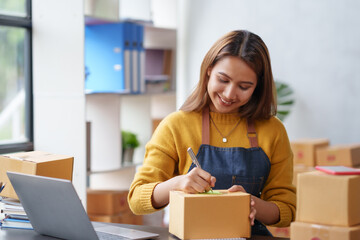 Smiling Asian online business owner prepares parcels and check online orders for delivery to customers on his laptop computer. Online selling concept.