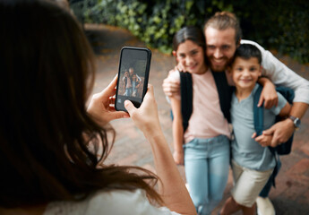 Mother taking a family photo on her phone of her happy little children and their father smiling...