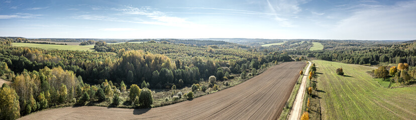 panoramic aerial view of agricultural fields and dirt road against blue sky on a bright sunny day